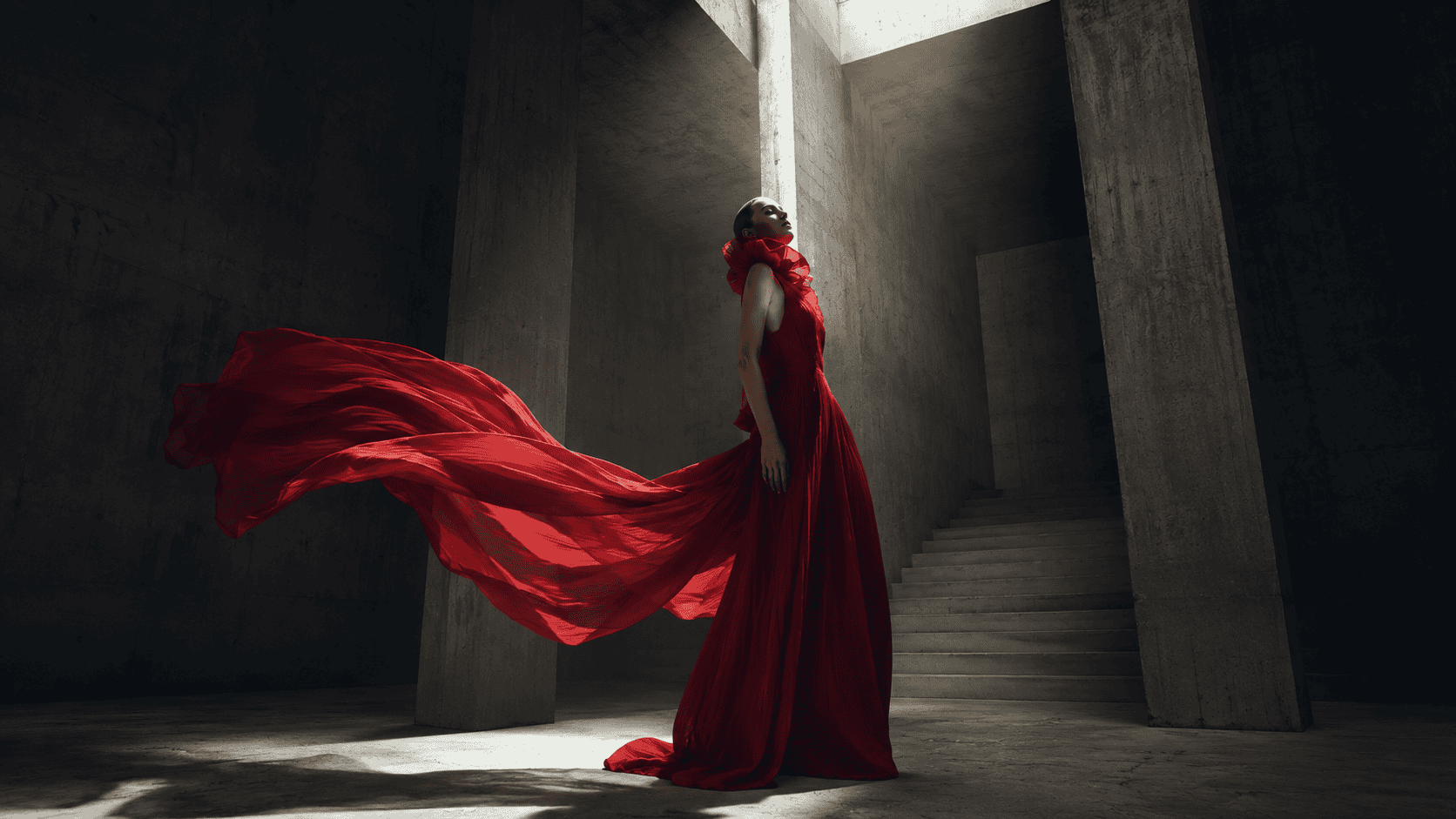 Woman in red dress standing in concrete structure with flowing fabric.