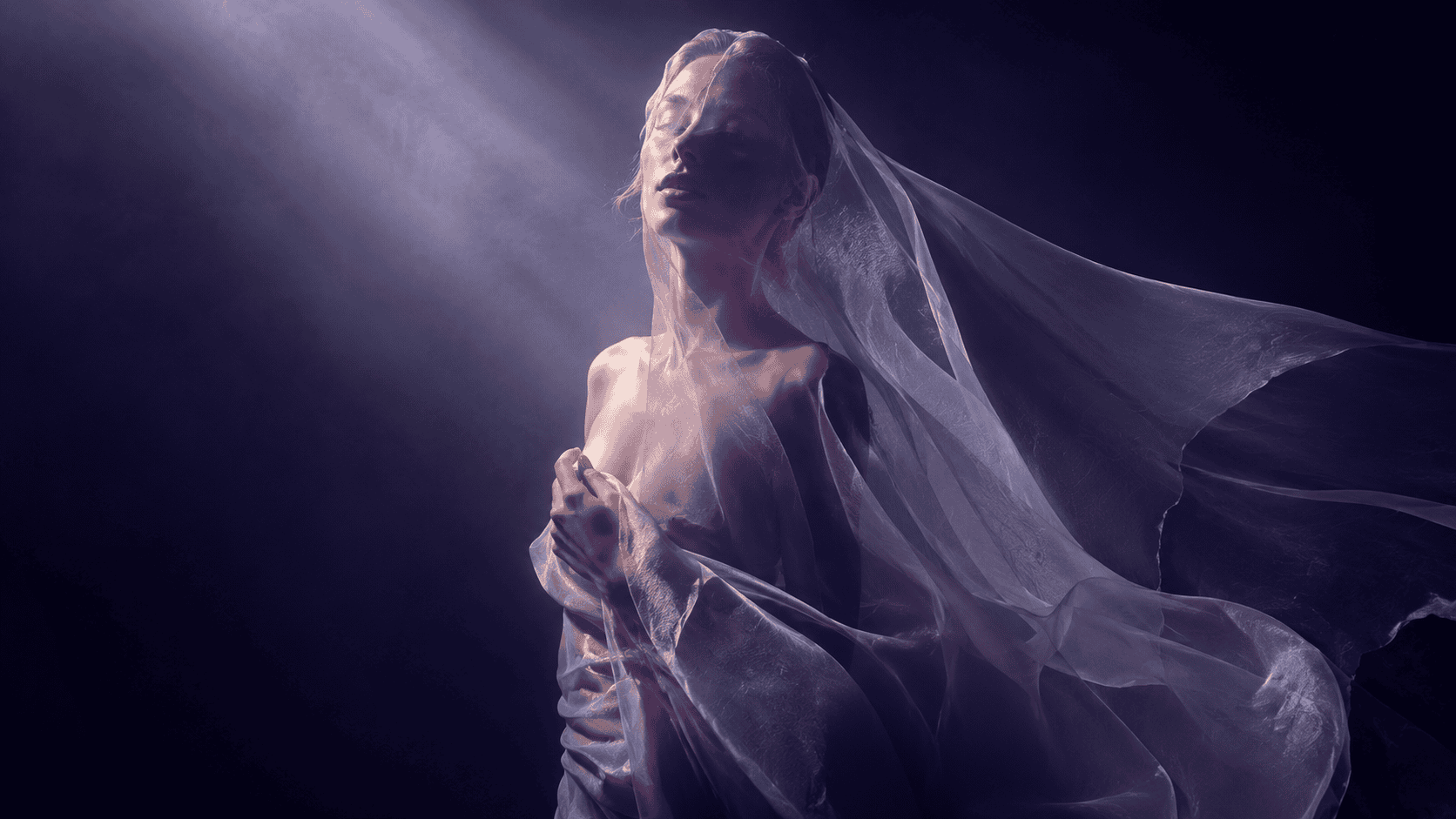 Female dancer in flowing fabric under dramatic spotlight, artistic fashion performance.
